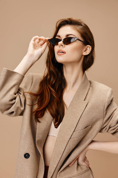 mujer en gafas de moda mirar a un lado en fondo beige y estilo de moda chaqueta - Foto, imagen