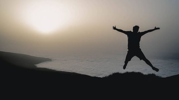 Una silhouette di un uomo che salta con vista sul tramonto sullo sfondo - Foto, immagini