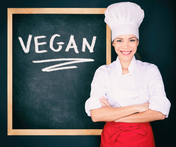 Vegan menu woman chef wearing uniform showing blackboard sign at restaurant for todays special. Vegeterian food. Word VEGAN handwritten on black chalkboard advert concept - Foto, Bild