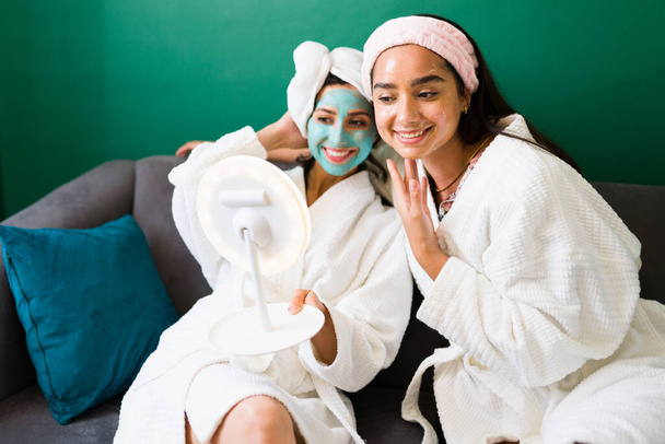 Ευτυχισμένες γυναίκες καλύτερες φίλες αισθάνονται καλά και θετικά, ενώ κοιτάζοντας στον καθρέφτη τα αποτελέσματα της ρουτίνας φροντίδας του δέρματος τους στο σπίτι - Φωτογραφία, εικόνα