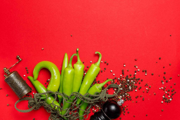 Pods of green hot pepper in a string bag,on a red background and peas of colored pepper, two spice mills on a red background, horizontal. with space - Photo, Image