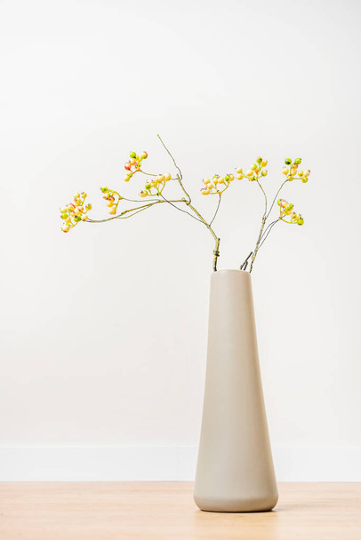 Hosszú szürke váza dekoratív éretlen áfonyás ágak fa padló és fehér háttér - Fotó, kép