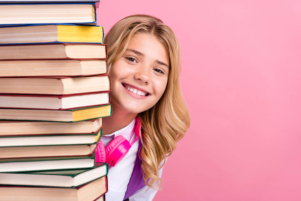 Portrait of attractive cheerful girl hiding behind stack book copy space isolated over pink pastel color background - Foto, Imagen