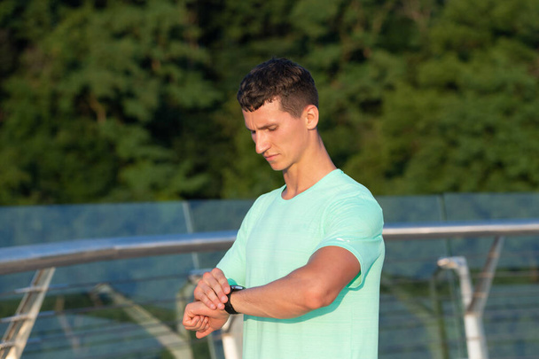 Atletische man controleren tijd op polshorloge tijdens outdoor training, sport timing - Foto, afbeelding