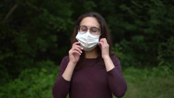 Egy szemüveges fiatal nő leveszi az orvosi maszkot és eldobja. Lány a természetben maszkban. - Felvétel, videó