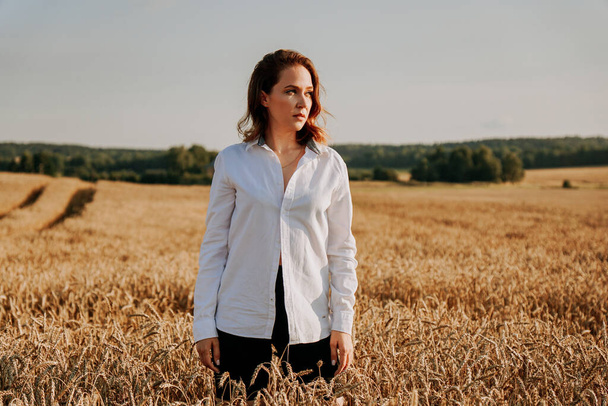 Portrait of red-haired girl in a white shirt. She in rye field on a sunny day - Photo, image