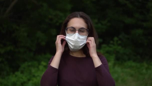 Eine junge Frau mit Brille nimmt eine medizinische Maske ab und wirft sie in die Kamera. Mädchen in der Natur in einer Maske. Zeitlupe. - Filmmaterial, Video