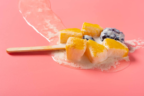 angle view melted homemade milk popsicle mixed with blackberry and blueberry and mango slices and pineapple slices on a pink background - Photo, Image