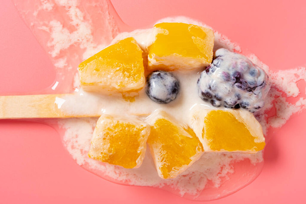 top view melted homemade milk popsicle mixed with blackberry and blueberry and mango slices and pineapple slices on a pink background - Photo, Image
