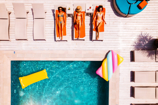 Друзі в купальнику, які засмагають у сонячному ліжку в басейні
 - Фото, зображення
