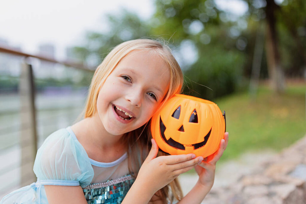 Little blonde Girl in costume of princess with Pumpkin lantern in park. Happy Halloween concept - Photo, Image