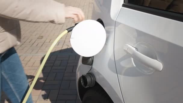 Женщина, приходящая к электрическому автомобилю и отключение кабеля питания для зарядки на улице в точке зарядки  - Кадры, видео