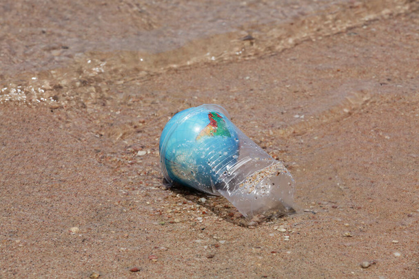 concept of environmental pollution. Planet Earth in plastic cup on the beach near sea. copy space. worldwide crisis of plastic pollution.  - Photo, Image