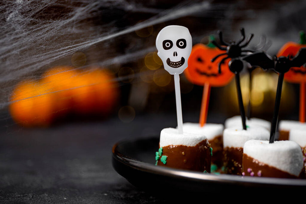  Sweet Halloween treat, chocolate covered marshmallows with sugar and Halloween decorations on a black plate, photo with soft focus and free space for text - Foto, Imagen