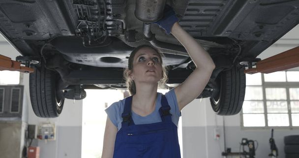 Female mechanic working under a car in the auto repair shop, she is checking for leaks - Φωτογραφία, εικόνα