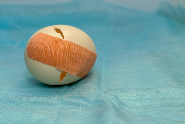 a cracked chicken egg is glued together with a medical plaster concept medical care. High quality photo - Foto, immagini