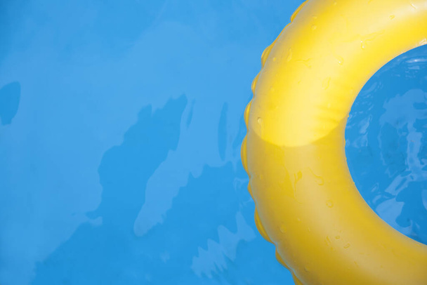 Detalle de anillo inflable amarillo flotando en piscina en día soleado. Vista superior. - Foto, Imagen