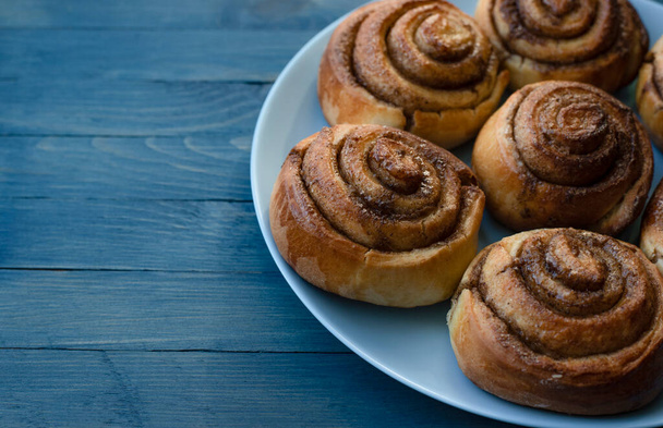 Homemade swirled rosy buns on a blue plate on the right on a blue wooden background - Valokuva, kuva