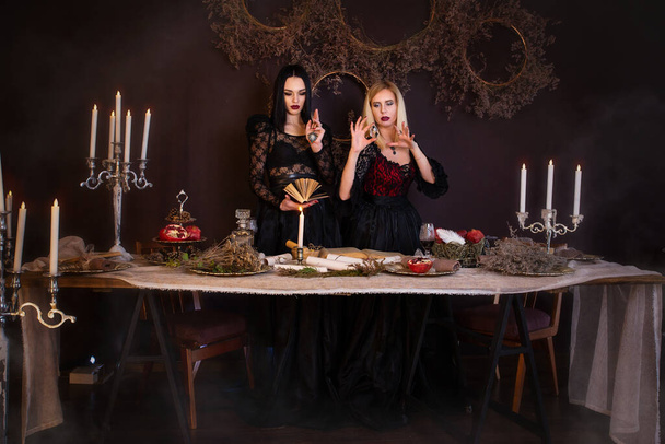 Чарівна, казка, чаклунка. Дві молоді красиві відьми виконують магічний ритуал свічками. Дві дівчини в красивих чорних сукнях. Хеллоуїн
 - Фото, зображення