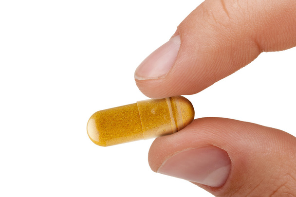 vingers een gele pil houden tegen ziekten op een witte achtergrond. - Foto, afbeelding