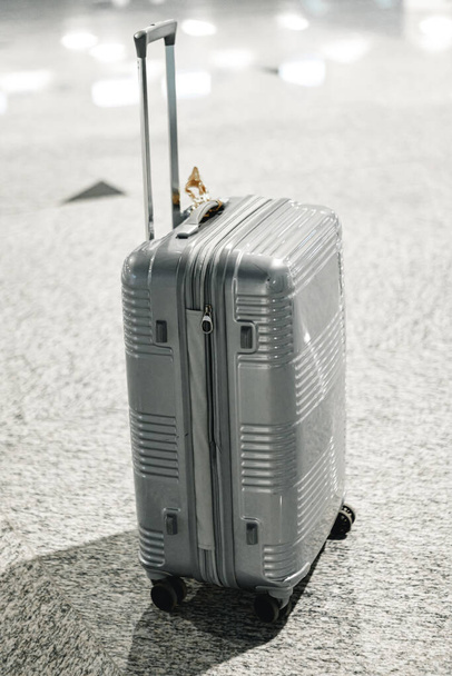Gray travel suitcase in empty airport hall - Foto, Imagen
