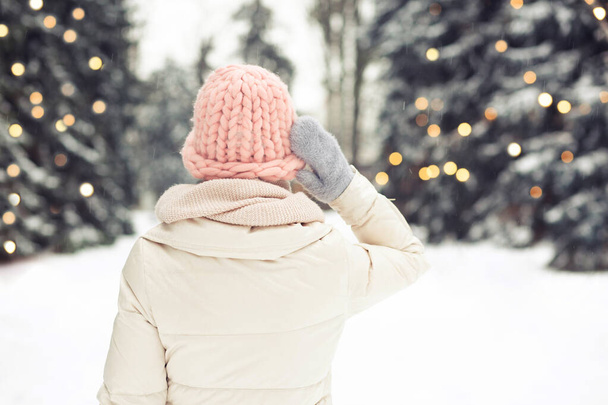 Mulher bonita usa roupa de inverno olhando para a floresta decorada com guirlandas. Espaço para texto - Foto, Imagem