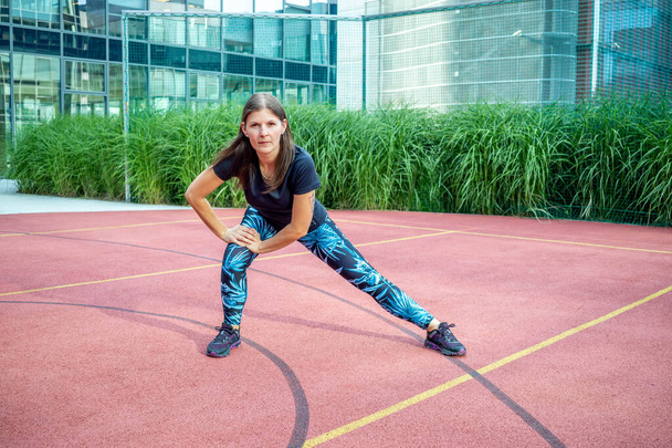 Jonge sportieve vrouw strekt zich uit in het park. Jonge vrouw aan het oefenen. Fitness en wellness workout concept. - Foto, afbeelding