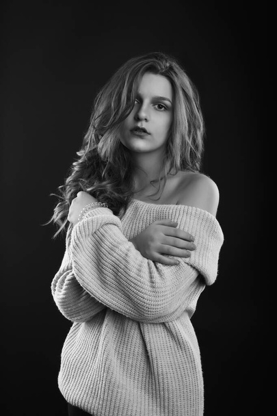 Cute brunette woman with long curly hair wears knitted sweater with naked shoulders posing in the shadow. Monochrome shot - Foto, immagini