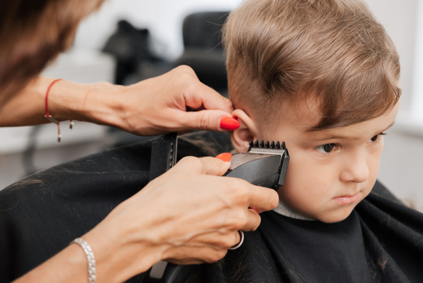 Dreharbeiten in einem Schönheitssalon. Ein Friseur schneidet einem kleinen Jungen mit einer Maschine die Haare. - Foto, Bild