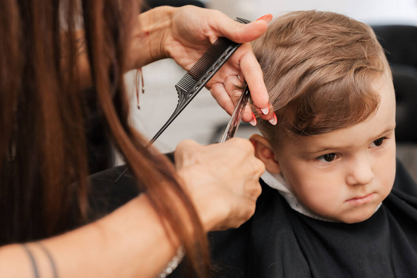 Dreharbeiten in einem Schönheitssalon. Ein Friseur schneidet einem kleinen Jungen mit der Schere die Haare - Foto, Bild