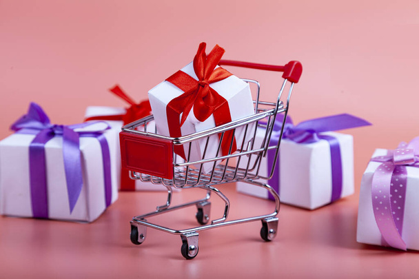 Shopping cart and gifts on a pink background. Concept: buying gifts. - Photo, Image