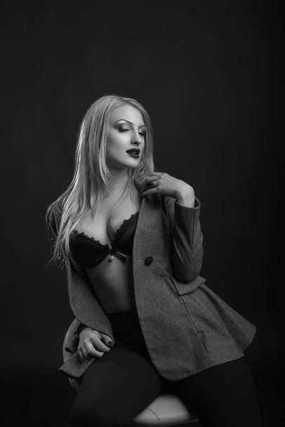 Sexy young lady wears bra and jacket posing at dark studio. Monochrome shot - Foto, afbeelding