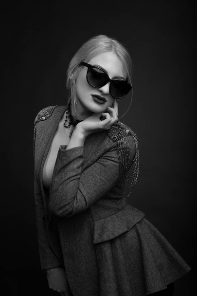 Schwarz-weißes Studioporträt einer fabelhaften blonden Frau, die Sonnenbrille und Jacke auf einem nackten Körper trägt - Foto, Bild
