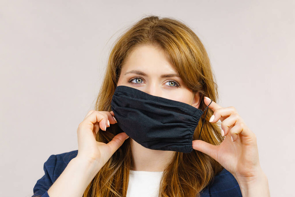 Woman using black protective reusable face mask, covering mouth. Coronavirus prevention. Health and safety. - Фото, зображення