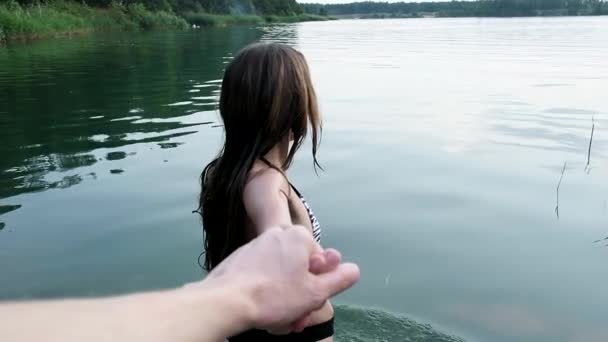 Bikinili çekici genç kız göle yavaşça girer ve erkeklerin elini tutar. - Video, Çekim