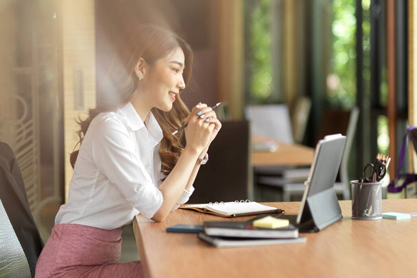 Young female manager feeling happy with her work, online meeting, online work interview with digital tablet and office supplies on wood table - Photo, Image