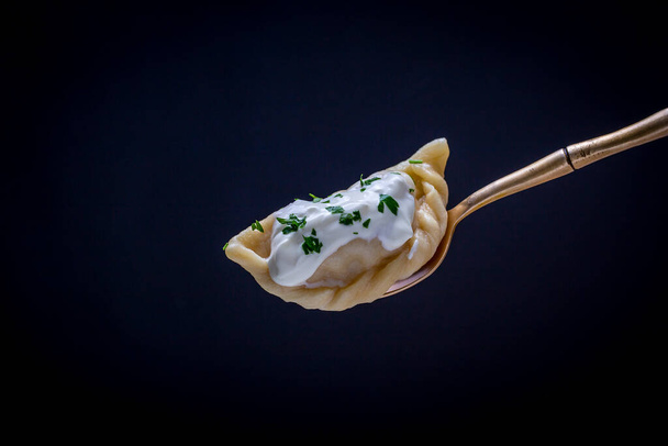 Ukrainian and Russian dishes - vareniki or dumplings with mashed potatoes or cottage cheese, sour cream and parsley on fork on black background, close up - Foto, immagini