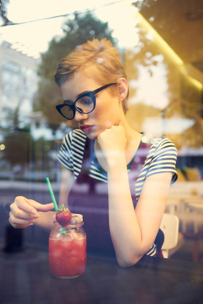 vrouw in bril met kort haar zit in een cafe eenzaamheid cocktail rest - Foto, afbeelding