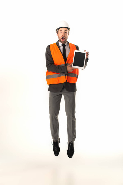 Ingeniero sorprendido sosteniendo tableta digital mientras salta aislado en blanco  - Foto, Imagen