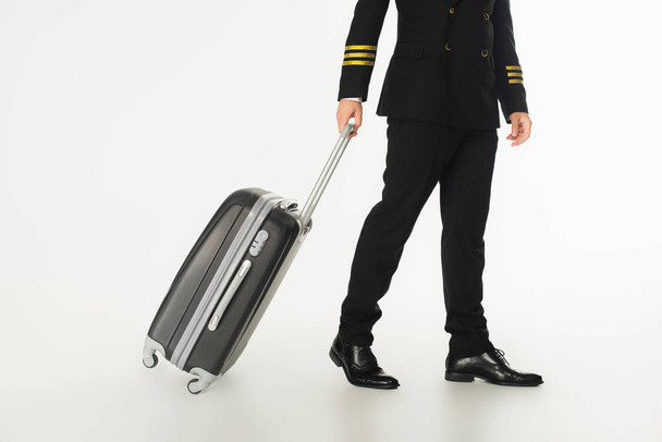Cropped view of pilot with suitcase walking on white background  - Фото, изображение