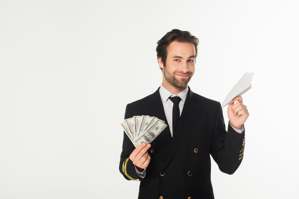 Pilota sorridente in possesso di aereo di carta e dollari isolati su bianco  - Foto, immagini