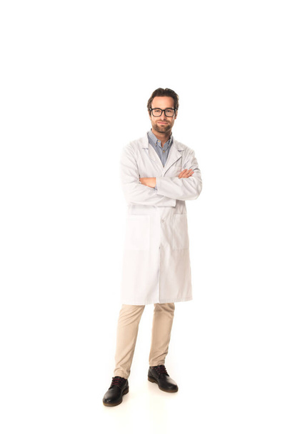 Full length of doctor standing with crossed arms on white background  - 写真・画像