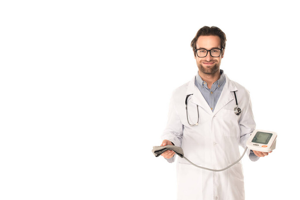 Sonriente médico sosteniendo tonómetro y mirando a la cámara aislada en blanco  - Foto, imagen