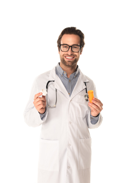 Позитивный доктор держит банку остроумия таблетки и колпачок изолирован на белом  - Фото, изображение