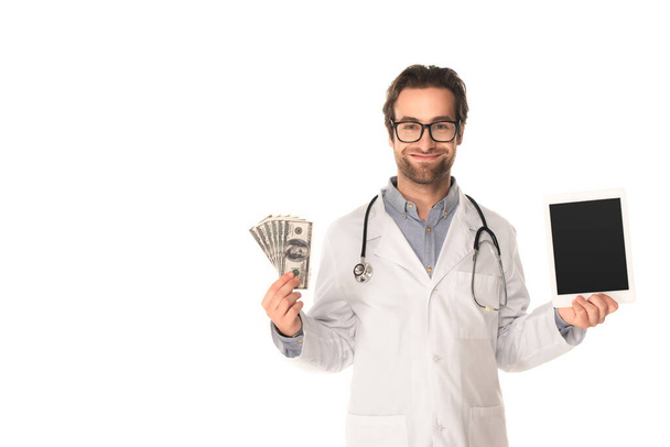 Smiling doctor holding digital tablet and money isolated on white  - Valokuva, kuva