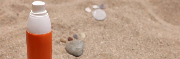 Orange jar of sunscreen standing on sand near stone footprints closeup - Photo, Image