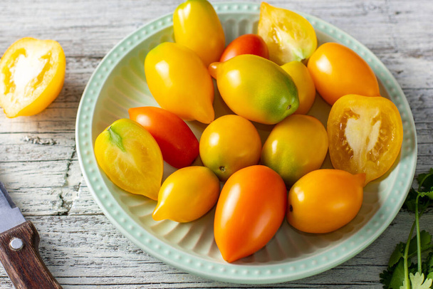 verschillende kleurrijke rijpe tomaat op witte houten achtergrond. Koken van gele sinaasappel en rode kerstomaten op de plaat - Foto, afbeelding