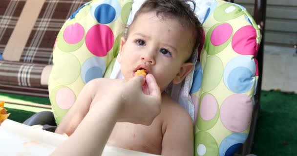 Ein kleines Kind sitzt auf einem Babystuhl und isst im Sommer einen Pfirsich. Kindheitskonzept. Nahaufnahme - Filmmaterial, Video
