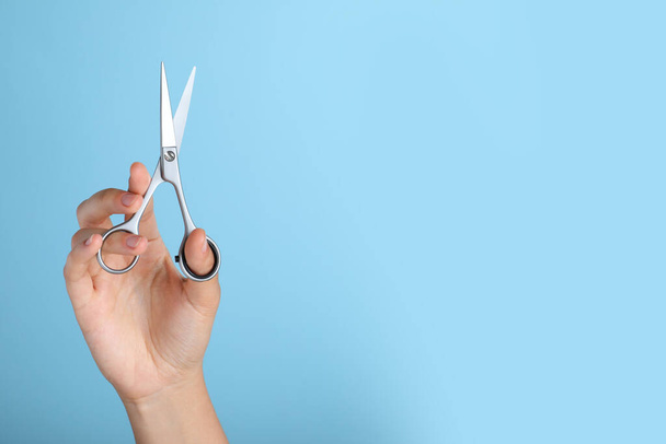 Hairdresser holding professional scissors and space for text on turquoise background, closeup. Haircut tool - Fotó, kép