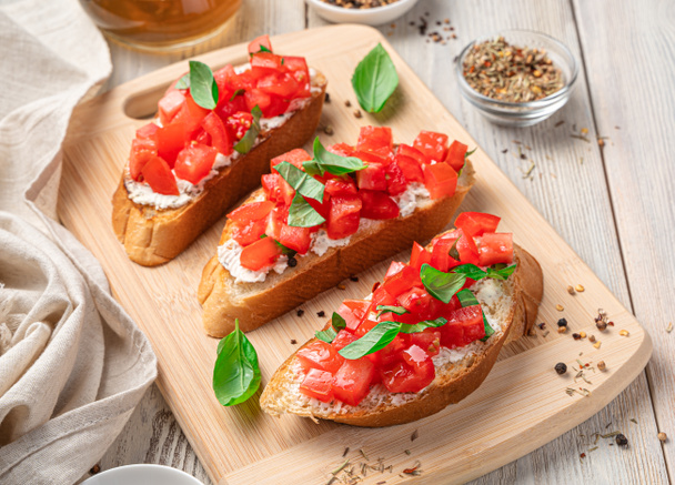 トマト、フェタ、バジル、伝統的なブルスケッタでサンドイッチ。軽い木の背景にイタリアの軽食. - 写真・画像